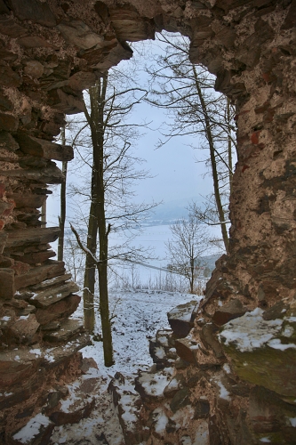 průhled dírou v hradní zdi na zasněženou krajinu se stromy