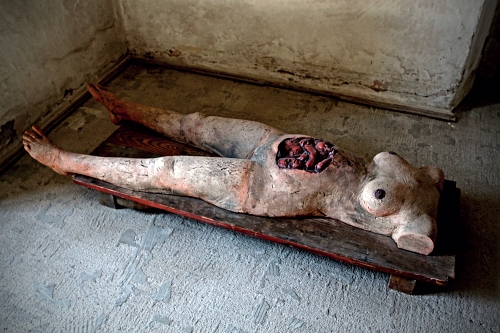 figurína ženy s rozpáraným břichem a vyhřezlými střevy